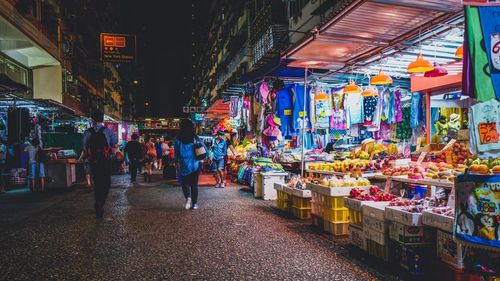 People walking on footpath in illuminated market at night