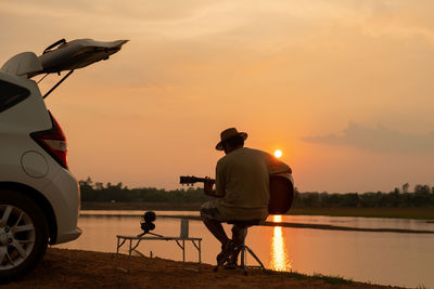 Rear view of man with umbrella on beach against sky during sunset