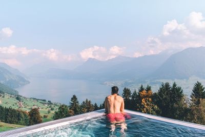 Rear view of shirtless man looking at swimming pool against sky