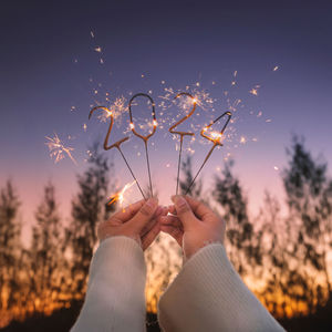 Cropped hand of woman holding sparkler against sky