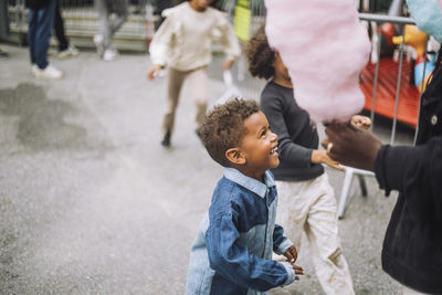 Excited boy looking at mother holding cotton candies at amusement park