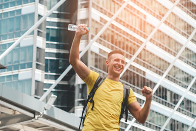 Young man smiling while standing against building in city