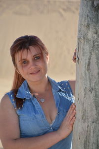 Portrait of young woman standing by tree trunk