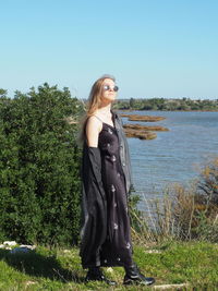 Young woman standing by plants against sky