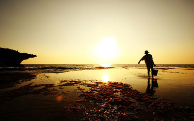 Silhouette man standing on beach against sky during sunset