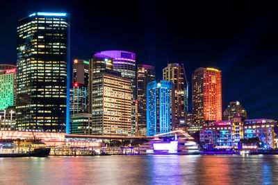 Illuminated buildings by river against sky in city at night