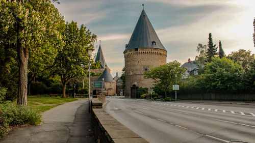 Road amidst trees and buildings against sky