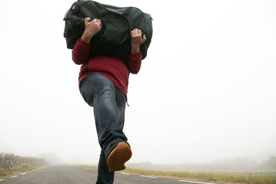 Carrying a suitcase in his arms an unrecognizable man walking along a road on a foggy day