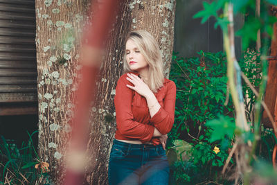 Young woman hugging self while standing against plants and tree