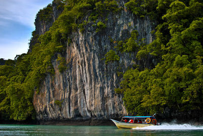 People in motorboat sailing on sea against cliff