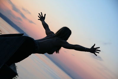 Topless woman with arms outstretched on pier by sea against sky during sunset