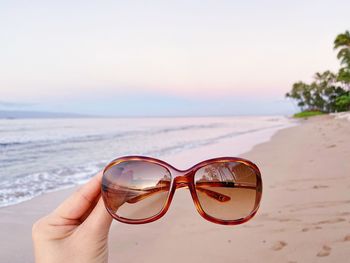 Close-up of hand holding sunglasses on beach