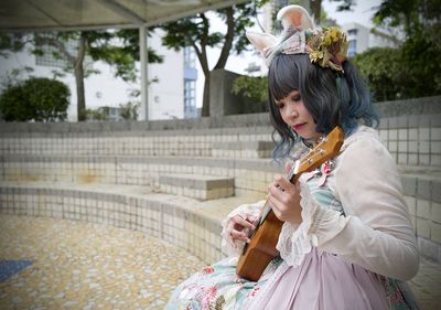 Full length of woman playing ukelele sitting outdoors