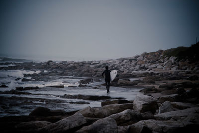 Rear view of woman standing on beach against clear sky