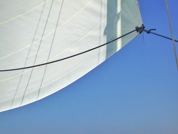 Low angle view of canvas on sailboat against clear blue sky