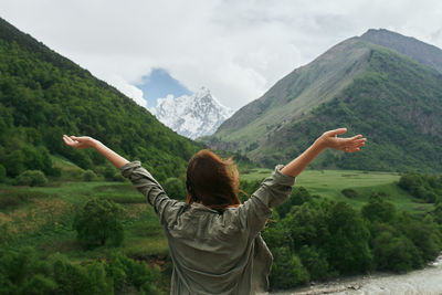 Rear view of woman with arms outstretched against mountain range