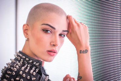 Portrait of young woman with shaved head standing against blue wall