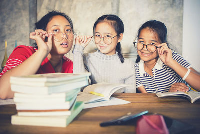 Portrait of smiling friends by books on table