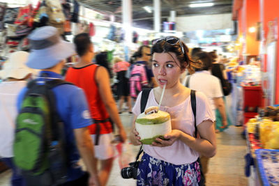 Young woman drinking coconut water in market at night