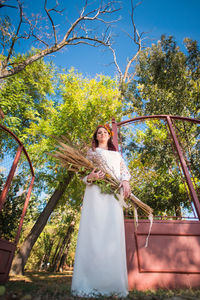 Portrait of young woman holding plants against trees