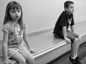 Siblings sitting on table against wall