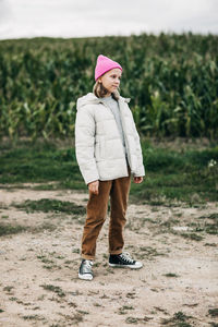 A teenage girl in a stylish image and a pink cap stands against the background of a corn field