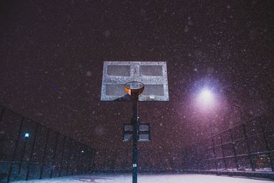 Illuminated street light on snow against sky at night