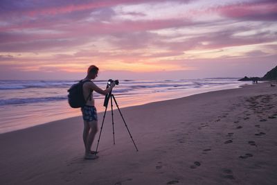 Man photographing at beach against sky during sunset