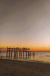 Silhouette wooden posts on beach against sky during sunset