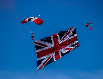 Low angle view of people paragliding with flag against clear blue sky