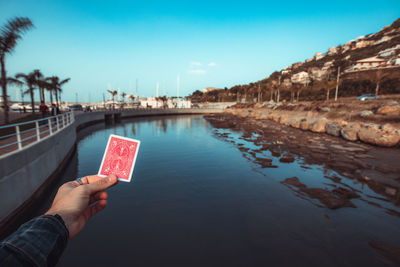 Midsection of person holding umbrella by river against sky