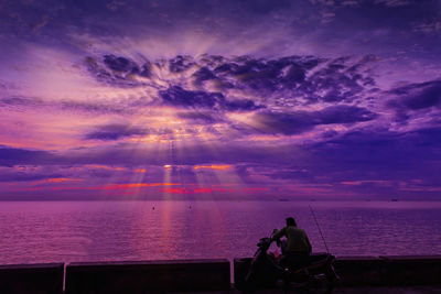 Rear view of man sitting on motor scooter by sea during sunset