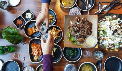 Cropped hands of friends toasting drinks over food in restaurant