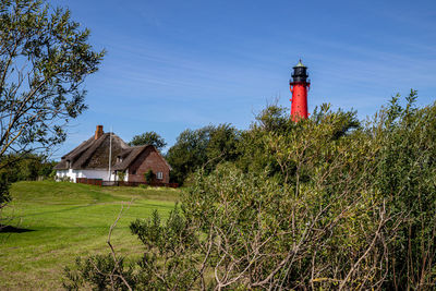 Lighthouse on field by building against sky