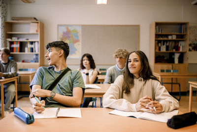 Boys and girls sitting with book on desk in classroom