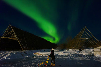 Woman standing on snow covered mountain against aurora polaris