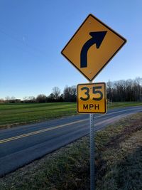 Road sign on field against clear blue sky