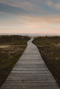 View of boardwalk on landscape against sky during sunset