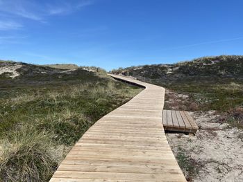 Boardwalk leading towards landscape against blue sky