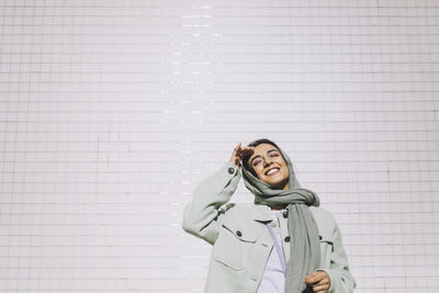 Happy woman wearing headscarf standing with eyes closed against wall