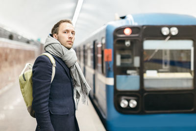 Handsome man in coat and with backpack who missed train. on background the train leaving platform.