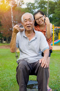 Portrait of grandfather by girl sitting on swing at park