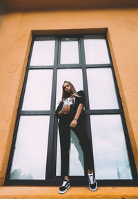 Full length portrait of woman standing by window