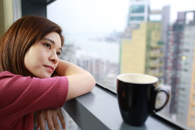 Close-up of woman sitting by window with coffee cup