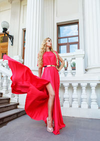 Fashionable woman with red gown standing outside building