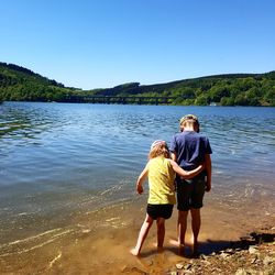 Siblings in lake against clear blue sky