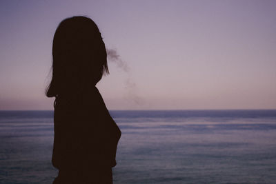 Silhouette woman standing at beach against sky during sunset