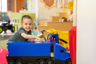 A happy smiling toddler boy plays with a big blue car in a children's entertainment center.