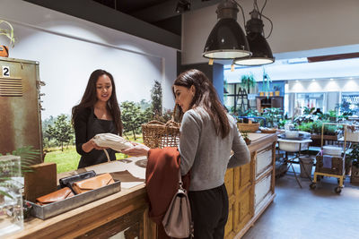 Saleswoman showing packet to female customer at checkout counter