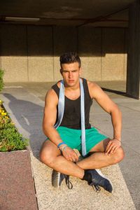 Portrait of fit young man sitting on retaining wall in city